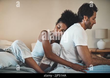 Woman tries to embrace her husband with affection after their fight at home. Unhappy interracial couple with marriage problems forgive each other Stock Photo