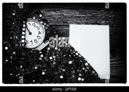 Black and white vintage image. An empty letterhead on an old wooden table next to a clock and a shiny festive fabric with silver sequins. Holiday conc Stock Photo