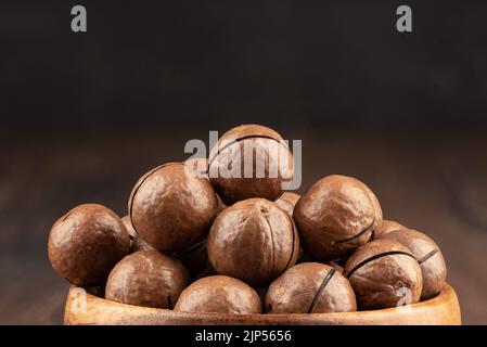 Close-up of unpeeled macadamia nuts on a dark background. Macadamia is a genus of woody plants in the Proteaceae family. Copy space. Stock Photo