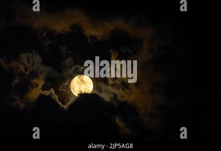 Full moon glow illuminates clouds on dark night Stock Photo