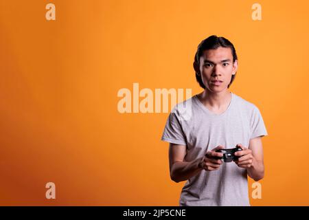 Young asian man playing video games with wireless gamepad, leisure activity, fun pastime. Teenager holding console controller gadget in hands, enjoying videogames with joystick Stock Photo
