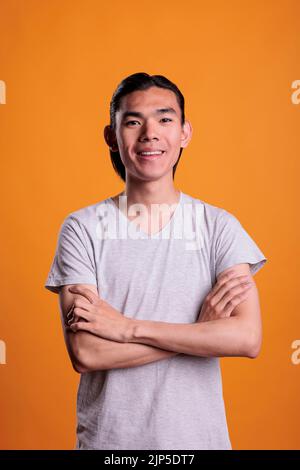 Young smiling happy asian man standing with arms crossed, looking at camera, front view. Cheerful teenager with positive facial expression portrait, attractive person medium shot Stock Photo