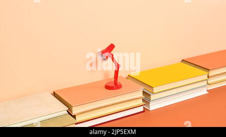 Creative red minimal table lamp on hardcover vintage books on two shade orange background. Flat lay Stock Photo