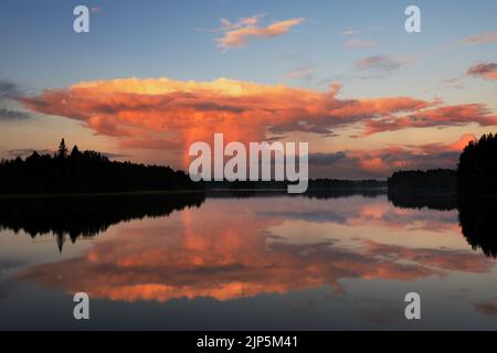 Anvil cloud lit by the setting sun. Cumulonimbus cloud rising over landscape in summer. Cloud reflection on water. Stock Photo