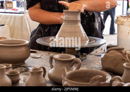 A potter man working on a potter's wheel making a ceramic pot out of clay. Master class on modeling on a potter's wheel. A few pots and jars not finis Stock Photo