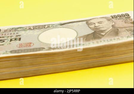 Ten thousand yen (10,000 yen) banknotes stacked. Japanese money. Paper money. Isolated on yellow background. Side view. Stock Photo