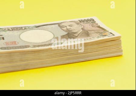 Ten thousand yen (10,000 yen) banknotes stacked. Japanese money. Paper money. Isolated on yellow background. Side view. Copy space. Stock Photo