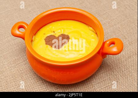 Homemade sweet corn pudding known in Brazil as Curau or Canjica Nordestina in ceramic bowl. Powdered cinnamon in the heart shape. Stock Photo