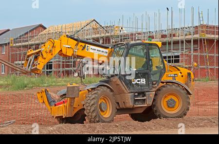 Development building site - JCB 535-125 construction Loadall  telehandler working in front of new properties surrounded by scaffolding Stock Photo