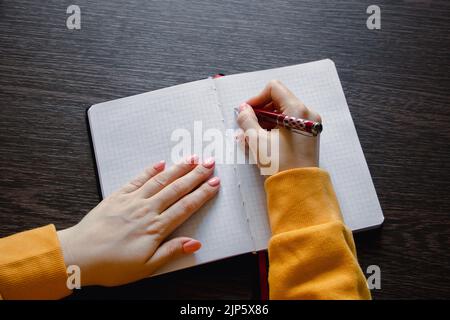 Woman writing in blank notebook. Close-up of hand holding pen. Businesswoman takes notes in office. Stock Photo