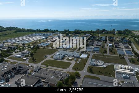 An aerial view above a vast, waterfront water treatment plant, seen during the day.
