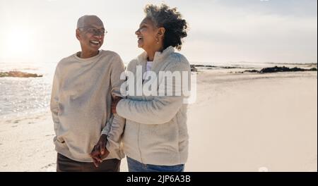 Romantic senior couple laughing together while taking a refreshing walk along the beach. Happy elderly couple couple enjoying their retirement days to Stock Photo