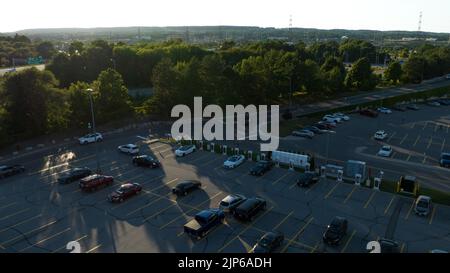 An aerial view looking at a Tesla Supercharger station in a parking lot as the evening shines through in the background. Stock Photo