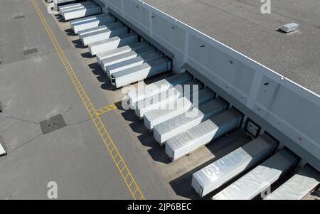 An aerial view above white trailers parked at a large warehouse, loading docks. Seen on a sunny day from a high, angled view. Stock Photo