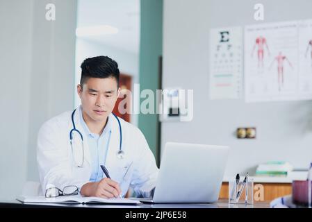 Checking his appointments. a young male doctor making notes while working in a hospital. Stock Photo