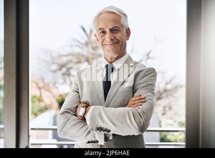 Making success happen. Portrait of a confident mature businessman wearing a business suit while standing with his arms folded at home during the day. Stock Photo