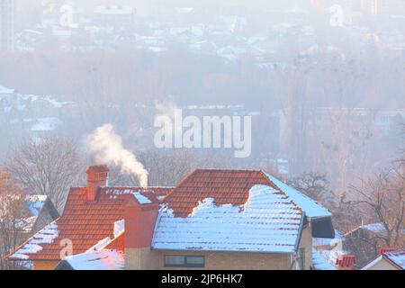 Chimney with smoke and tiled roof . Cottage with snowy rooftop Stock Photo