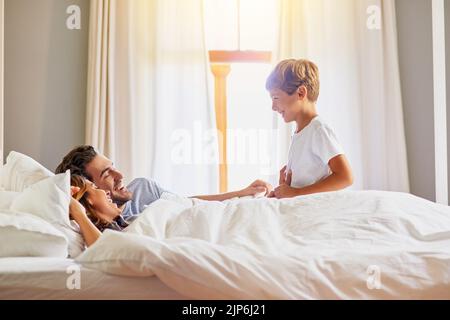Are we still going out today. a cheerful little boy trying to wake up his family in bed at home in the morning. Stock Photo
