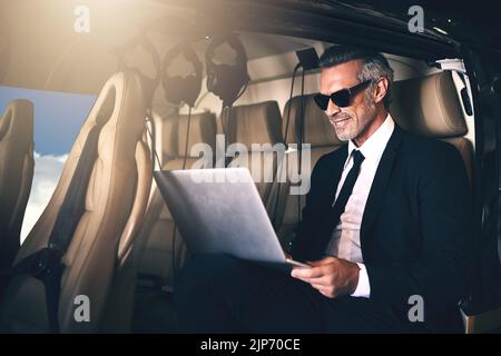 Success is in the air. a mature businessman using a laptop while traveling in a helicopter. Stock Photo