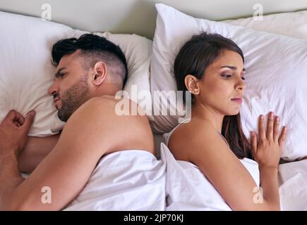 Turning their back to each other and their problems. a young married couple angry at each other in their bed at home. Stock Photo