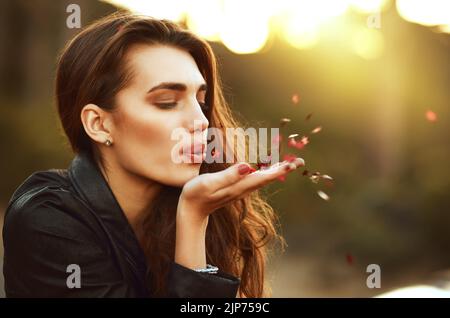 Beauty so magical. an attractive young woman blowing confetti from her hand outdoors. Stock Photo