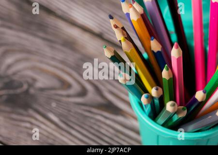 Colored pencils for drawing.  They stand in a pencil holder in the form of a trash can. On pine boards.  Close-up. Stock Photo