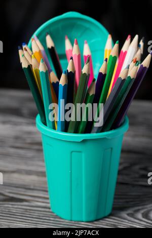 Colored pencils for drawing.  They stand in a pencil holder in the form of a trash can. On pine boards. Stock Photo