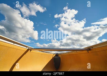 A view from low in the hull of a canoe shows a blue sky with fluffy white clouds above the bow of the canoe. Stock Photo
