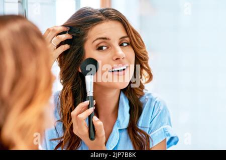 Blush is a must. a beautiful young woman applying blush on to her cheeks at home. Stock Photo