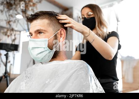 Hairdresser trimming the hair of a client with facial mask Stock Photo