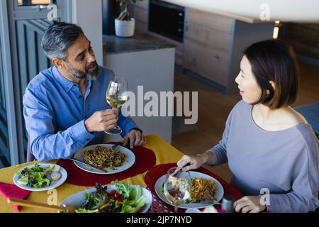 Happy diverse couple sitting at table, eating dinner together Stock Photo