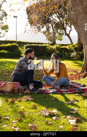 Romantic caucasian couple sitting on rug having picnic in sunny autumn garden Stock Photo