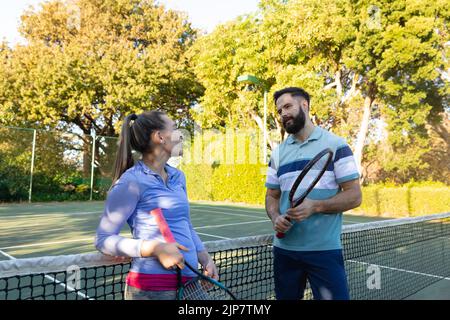 Caucasian couple playing tennis talking on outdoor tennis court Stock Photo