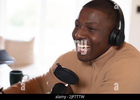 Laughing african american man making podcast at home wearing headphones Stock Photo