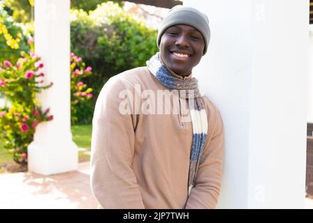 Portraif of smiling african american man at home sitting in garden wearing hat and scarf Stock Photo