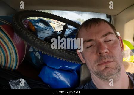 view of the face of a tired, sleeping person in the back seat of a car after a difficult bike ride Stock Photo