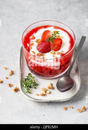 Homemade delicious strawberry puree and cream cheese layered dessert decorated with fresh berries, granola and sprig of thyme in a glas bowl. Healthy Stock Photo