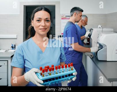 Diagnostic laboratory scientist holding test tube rack with blood samples near laboratory workers who conducts research on lab machines Stock Photo