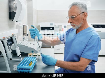 Mature male scientist with micropipette for test analyzes working at medical research laboratory. Laboratory technician determines person's blood type Stock Photo