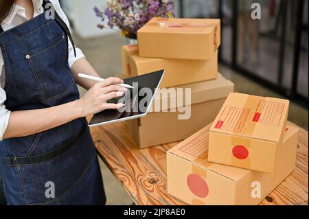 A female e-commerce business owner working in her office, using digital tablet to check her shipping orders. cropped and close-up image Stock Photo