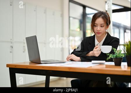 Thoughtful young Asian businesswoman having a coffee while pensive thinking a business strategy plan for her project. Stock Photo