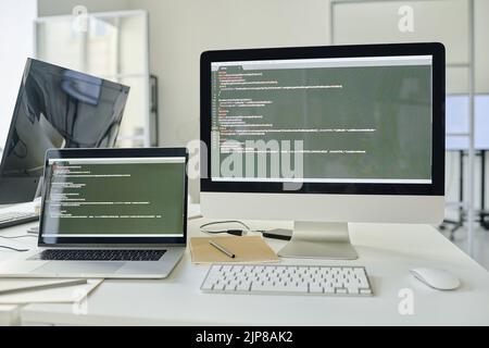 Horizontal image of workplace of programmer with computer and laptop with software on the screen Stock Photo