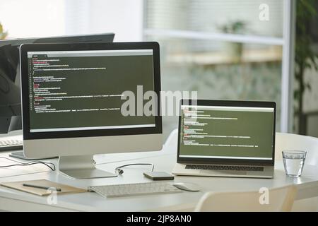 Horizontal image of workplace with computer and laptop ith codes on the screens on table at office Stock Photo