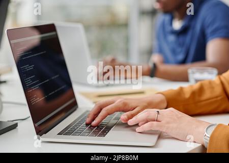 Close -up of female programmer typing codes on laptop during her work at office with colleagues Stock Photo