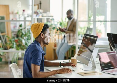 African young programmer concentrating on writing codes on new software while sitting at his workplace at office Stock Photo