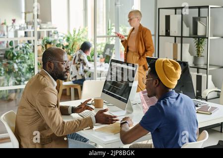 African programmers discussing software together while sitting at table with computer during meeting Stock Photo
