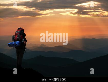 Evening silhouette - view of man on mountains with big rucksack on back Stock Photo