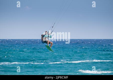 Man kitesurfing and jumping in the air with a young boy in his back  at the sea of Agiokampos beach , Greece Stock Photo
