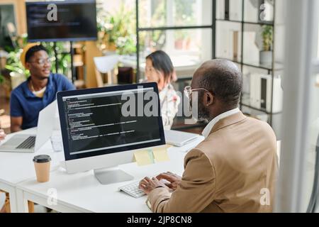 Rear view of African programmer writing code on computer sitting at his workplace at office Stock Photo