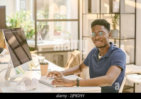 Portrait of African young programmer in eyeglasses looking at camera working at his workplace at office Stock Photo